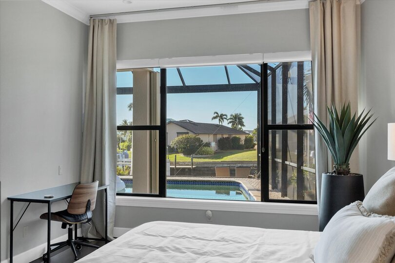 Primary bedroom features king bed, attached bathroom, desk & chair, 65-inch Smart TV, and beautiful view of pool and canal
